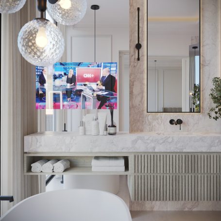 Baño moderno con espejo, mueble de lavabo y televisión encendida.